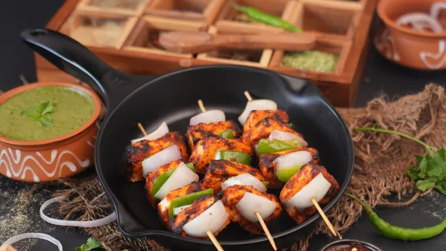 Grilled paneer tikka skewers in a pan with green chutney