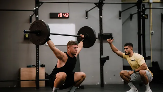 A lifter doing an overhead squat with a coach alongside